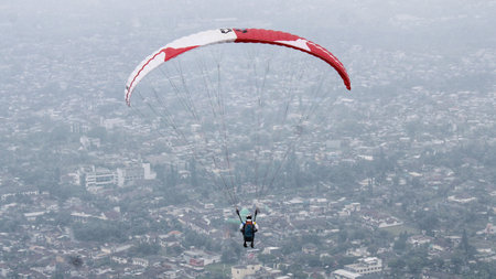 Paraglider pilot flying high in the sky with village viewの写真素材