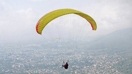 Paraglider pilot flying high in blue sky with village and mountain viewの写真素材