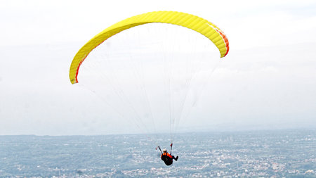 Paraglider pilot flying high in blue sky with village and mountain viewの写真素材
