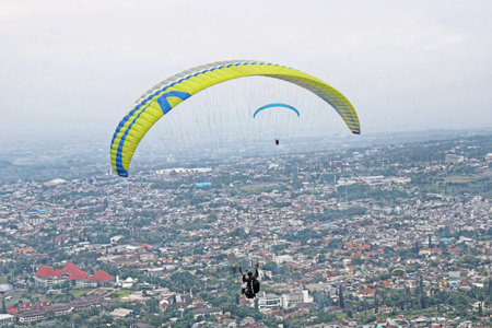 Paraglider pilot flying high in blue sky with village viewの写真素材