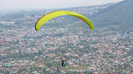 Paraglider pilot flying high in blue sky with village and mountain viewの写真素材