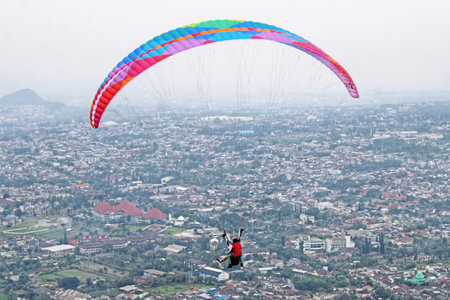 Paraglider pilot flying high in blue sky with village viewの写真素材