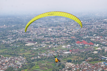 Paraglider pilot flying high in blue sky with village viewの写真素材