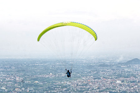 Paraglider pilot flying high in blue sky with village and mountain viewの写真素材