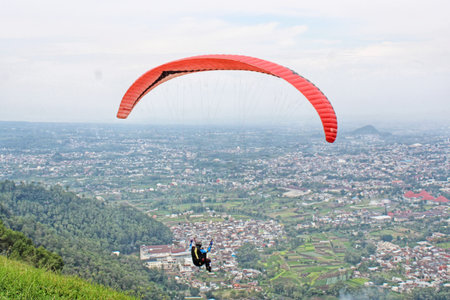 Paraglider pilot flying high in blue sky with village and mountain viewの写真素材