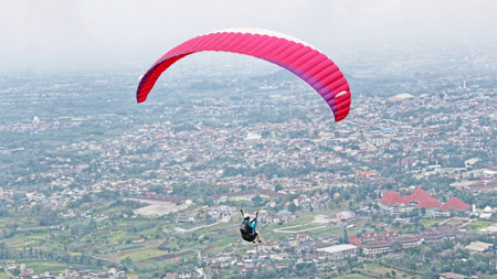 Paraglider pilot flying high in blue sky with village and mountain viewの写真素材