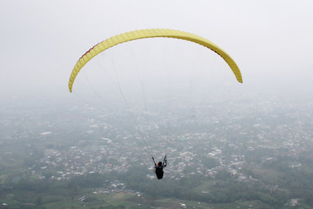 Paraglider pilot flying high in blue sky with village and mountain viewの写真素材