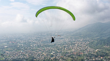 Paraglider pilot flying high in blue sky with village and mountain viewの写真素材