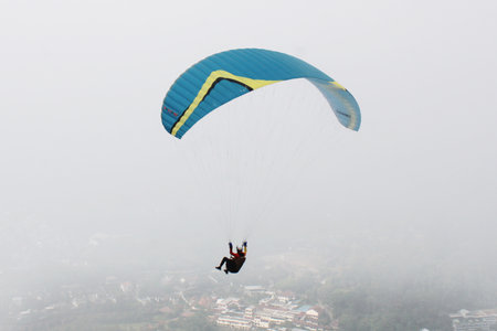 paragliding pilot flying in the blue sky with white cloudsの写真素材