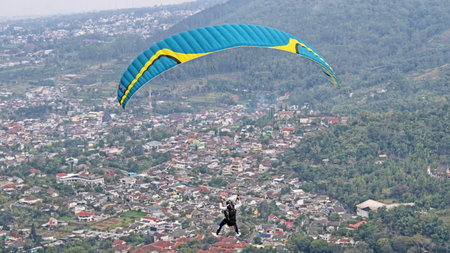 Paraglider pilot flying high in blue sky with village and mountain viewの写真素材