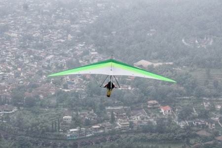 hang gliding flying high above with views of the village and blue sky in the backgroundの写真素材