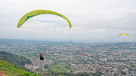 Paraglider pilot flying high in blue sky with village and mountain viewの写真素材