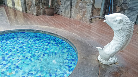 fish statues with fountain ornaments by blue swimming poolの写真素材