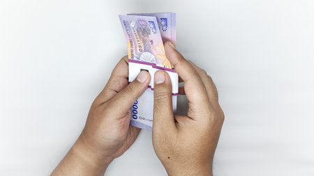 two hands holding Indonesian banknotes in the 10000 rupiah denomination