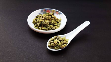 indian spice cardamom in bowl and spoon isolated on black background