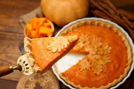 Traditional american fresh round bright orange homemade pumpkin pie in baking dish on wooden tableの写真素材