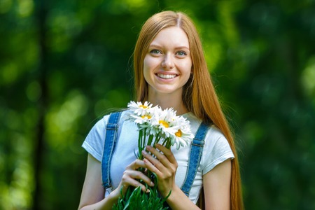 Portrait of beautiful caucasian smiling red-haired young woman, against summer green park.の写真素材