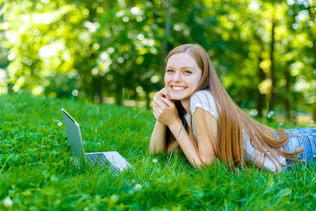Portrait of beautiful caucasian smiling red-haired young woman, against summer green park.の写真素材