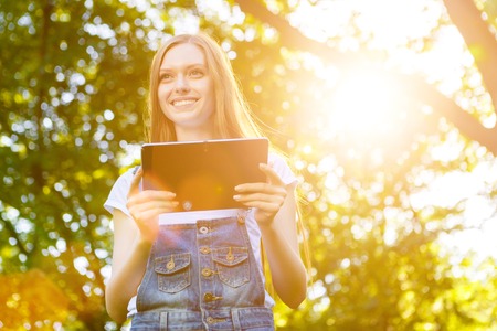 Portrait of beautiful caucasian smiling red-haired young woman, against summer green park.の写真素材