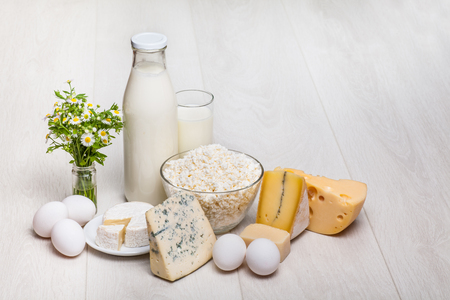 milk bottle and glass on wooden background, cottage cheese, eggs, camambert, Parmigiano, Roquefortの写真素材