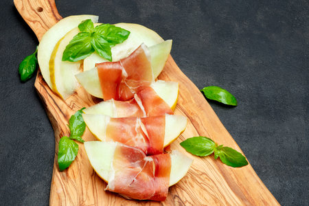 italian food with melon and prosciutto on wooden cutting boardの写真素材