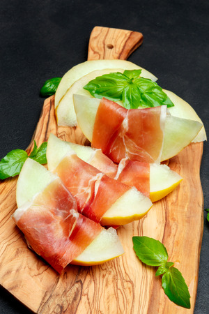 italian food with melon and prosciutto on wooden cutting boardの写真素材