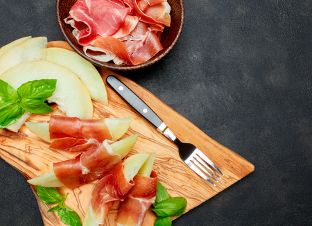 italian food with melon and prosciutto on wooden cutting boardの写真素材