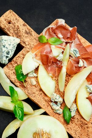 italian food with melon, prosciutto and cheese on cork cutting boardの写真素材