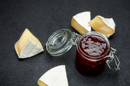 Jam of raspberries and pieces of brie cheese on dark concrete backroundの写真素材