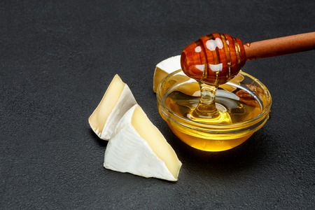 Honey and pieces of brie cheese on dark concrete backroundの写真素材