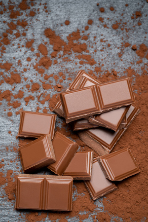 Dark or milk organic chocolate pieces and cocoa powder on dark concrete backgound