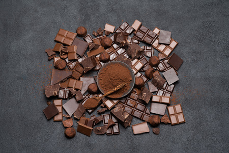 Dark or milk organic chocolate pieces, cocoa powder and truffle candies on dark concrete backgound