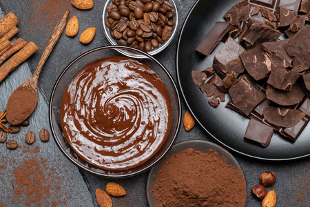 Melted chocolate or Hazelnut spread in glass bowl and chocolate pieces on dark concrete backgroundの写真素材