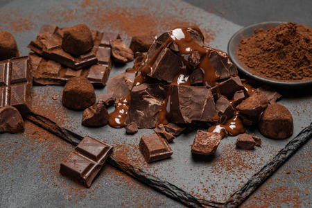 dark or milk chocolate pieces, chocolate syrup and truffle candies on dark concrete backgroundの写真素材