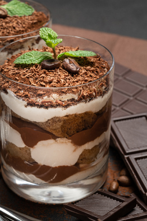 two portions Classic tiramisu dessert in a glass and chocolate bar on dark concrete backgroundの写真素材