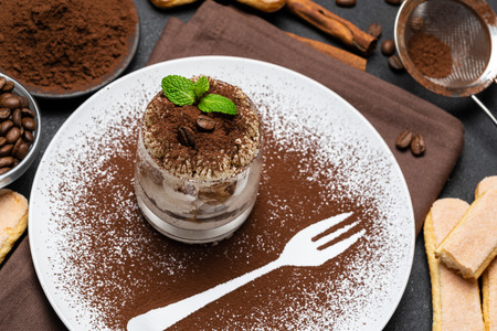 Classic tiramisu dessert in a glass and cup of coffee on dark concrete backgroundの写真素材