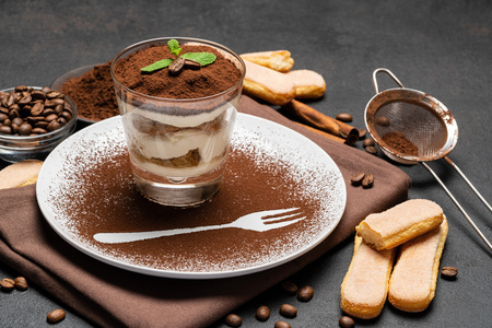 Classic tiramisu dessert in a glass and cup of coffee on dark concrete backgroundの写真素材