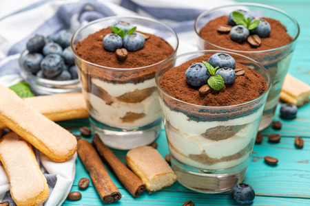 Classic tiramisu dessert in a glass with blueberries on blue wooden backgroundの写真素材