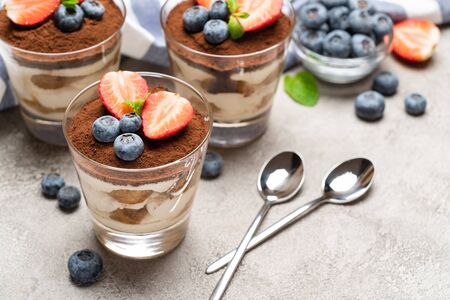 Classic tiramisu dessert with blueberries and strawberries in a glass on concrete backgroundの写真素材