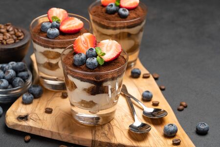 Classic tiramisu dessert with blueberries and strawberries in a glass on dark concrete backgroundの写真素材