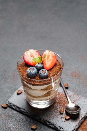 Classic tiramisu dessert with blueberries and strawberries in a glass on stone serving board on dark concrete backgroundの写真素材