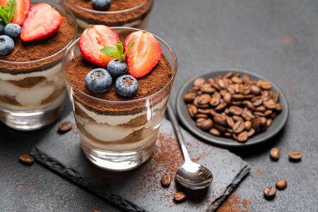 Classic tiramisu dessert with blueberries and strawberries in a glass on stone serving board on dark concrete backgroundの写真素材