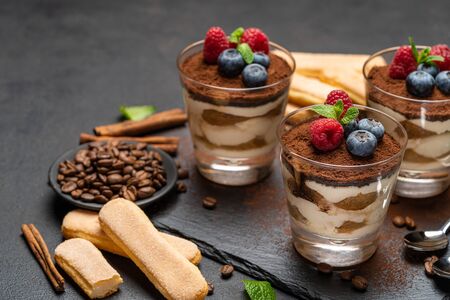 Classic tiramisu dessert with blueberries and raspberries in a glass and savoiardi cookies on stone serving board on dark concrete backgroundの写真素材
