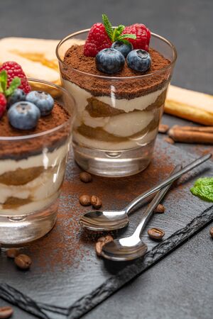 Classic tiramisu dessert with blueberries and raspberries in a glass and savoiardi cookies on stone serving board on dark concrete backgroundの写真素材