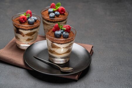 Classic tiramisu dessert with blueberries and raspberries in a glass on dark concrete backgroundの写真素材