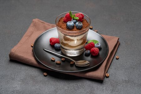 Classic tiramisu dessert with blueberries and raspberries in a glass on dark concrete backgroundの写真素材