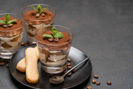 Classic tiramisu dessert in a glass and savoiardi cookies on dark concrete backgroundの写真素材