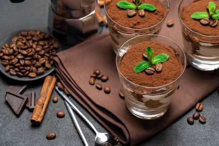 Classic tiramisu dessert in a glass and coffee maker on dark concrete backgroundの写真素材