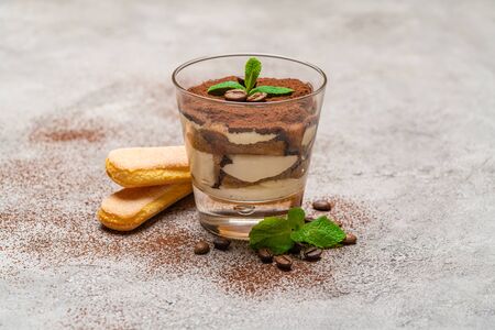 Classic tiramisu dessert in a glass cup and savoiardi cookies on concrete background