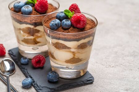 Classic tiramisu dessert with blueberries and raspberries in a glass on stone serving board on concrete backgroundの写真素材